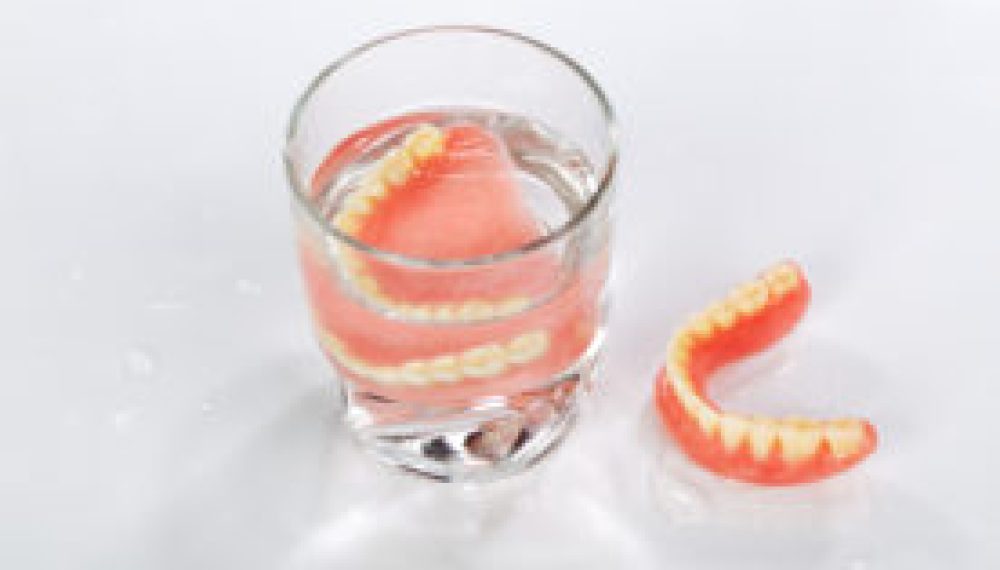 A set of dentures in a glass of water on a white background A set of dentures in a glass of water on a white background